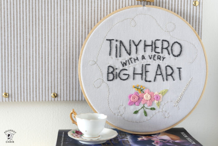 embroidery hoop on book with teacup leaning against pin board