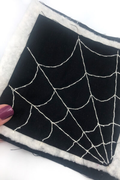 black fabric with a white spiderweb stitched with white thread on white table