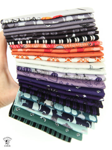 hand holding a stack of halloween fabrics in gray, orange, ivory and green
