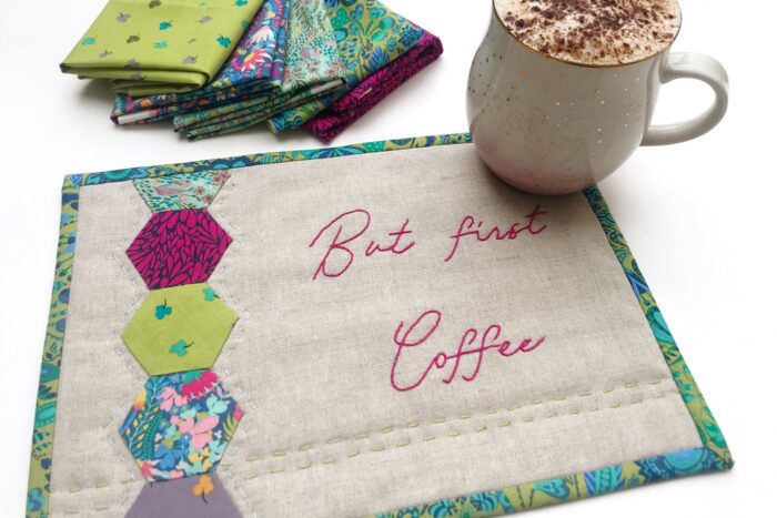 tan and jewel tone mug rug on white table with coffee and fabric