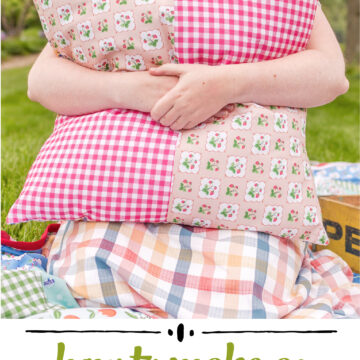 girl holding a colorful giant pillow outdoors on a picnic blanket