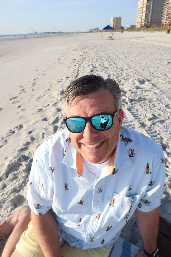 man sitting on beach wearing sunglasses