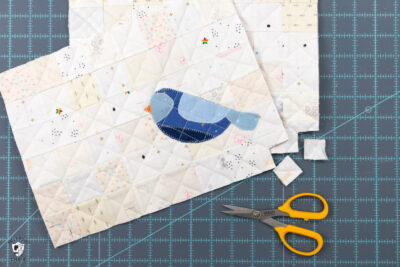 blue bird sewn to patchwork grid of white and cream squares with scissors