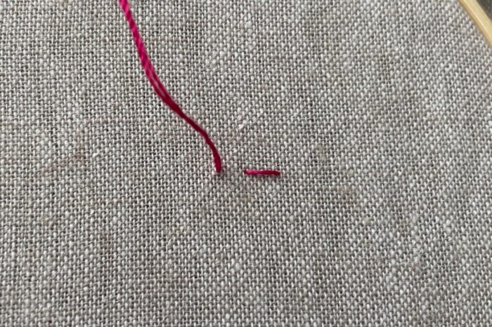 red embroidery thread on needle on canvas